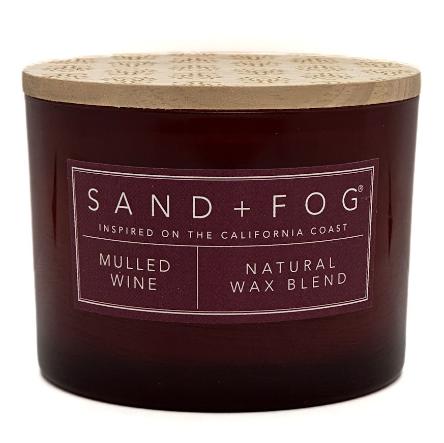 A dark red glass jar candle with a light wood lid, featuring a label that reads 'SAND+FOG' and 'MULLED WINE NATURAL WAX BLEND'.