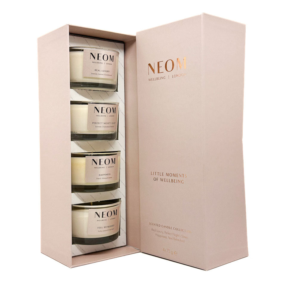 NEOM Wellbeing London 'Little Moments of Wellbeing' scented candle collection in a light pink gift box, containing four candles in clear glass jars with cream-colored wax and gold labels.