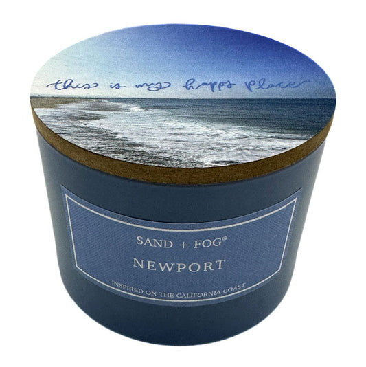 Candle container with beach scene lid and 'Sand + Fog Newport' label on a white background