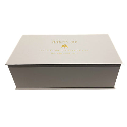 A rectangular presentation box for 'NINETY SIX' fragrances, featuring a light beige lid with gold foil lettering and a dark gray base, photographed on a clean white background.