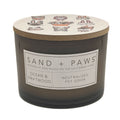 Candle with 'Sand + Paws' label and ocean and driftwood scent on a white background