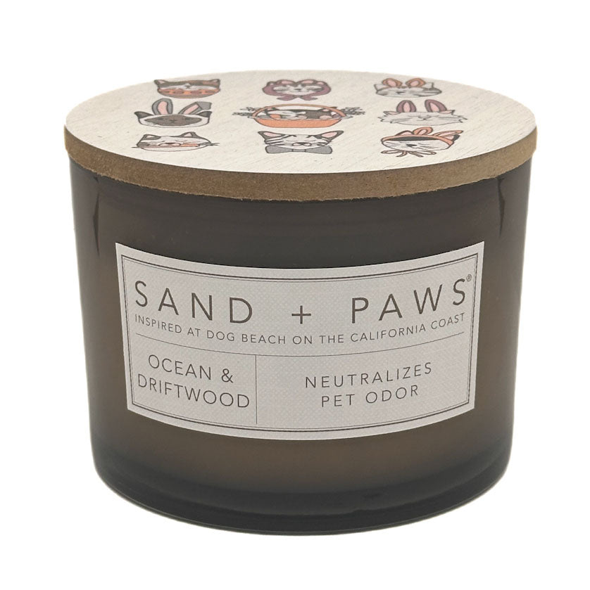 Candle with 'Sand + Paws' label and ocean and driftwood scent on a white background