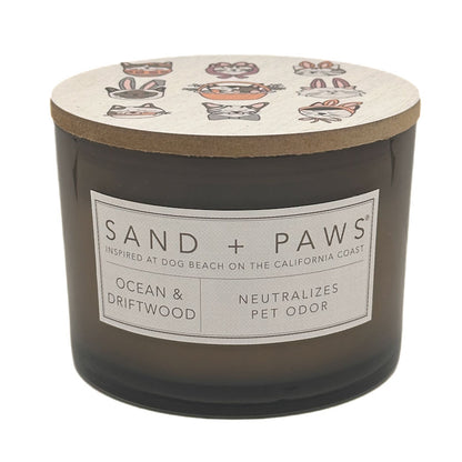 Candle with 'Sand + Paws' label and ocean and driftwood scent on a white background