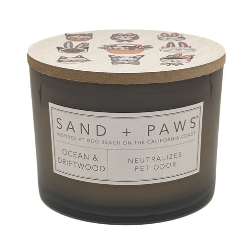 Candle with 'Sand + Paws' label and ocean and driftwood scent on a white background
