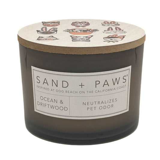 Candle with 'Sand + Paws' label and ocean and driftwood scent on a white background