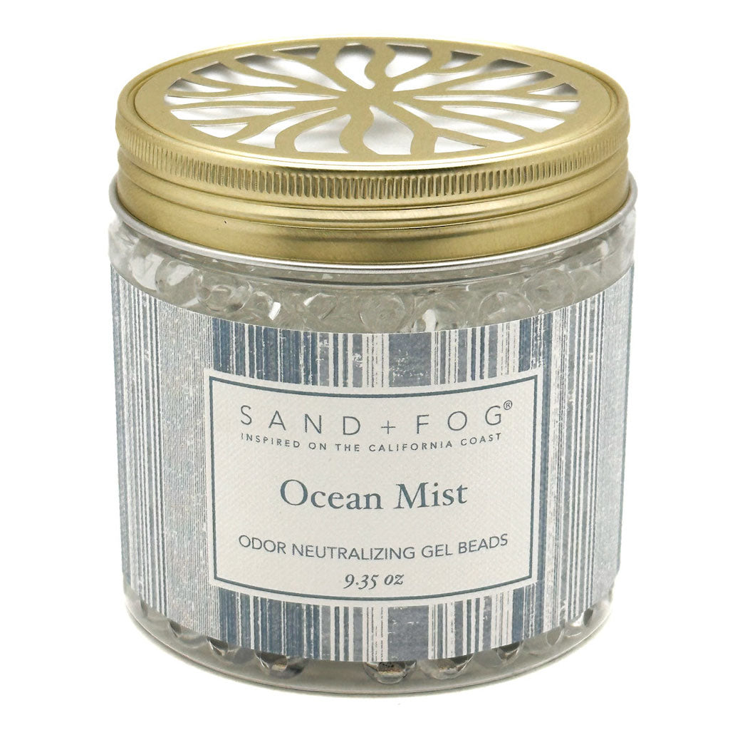 A jar of Sand + Fog Ocean Mist odour neutralising gel beads, featuring a metallic gold lid with a decorative cutout and a grey-white label.