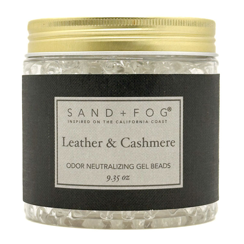 A jar of Sand + Fog Leather & Cashmere odor neutralizing gel beads, featuring a black label and a gold metal lid, filled with clear gel beads.