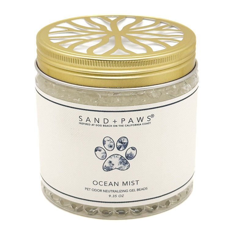 A jar of Sand + Paws Ocean Mist pet odor neutralizing gel beads with a gold metal lid and white label, set against a plain white background.