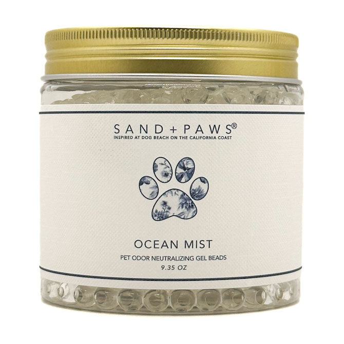 A jar of Sand + Paws Ocean Mist pet odor neutralizing gel beads with a gold metal lid and a white label featuring a blue paw print.