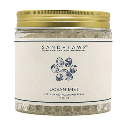 A jar of Sand + Paws Ocean Mist pet odor neutralizing gel beads with a gold metal lid and a white label featuring a blue paw print.