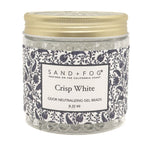 A jar of Sand + Fog Crisp White odor neutralizing gel beads, featuring a patterned navy and white label with a gold metal lid, on a white background.