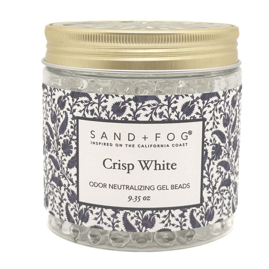 A jar of Sand + Fog Crisp White odor neutralizing gel beads, featuring a patterned navy and white label with a gold metal lid, on a white background.