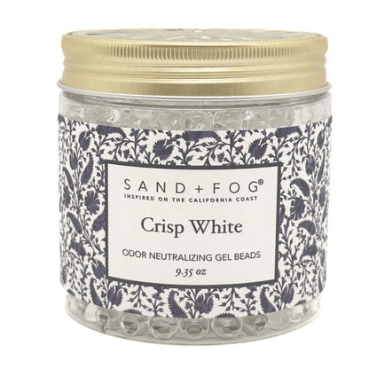 A jar of Sand + Fog Crisp White odor neutralizing gel beads, featuring a patterned navy and white label with a gold metal lid, on a white background.