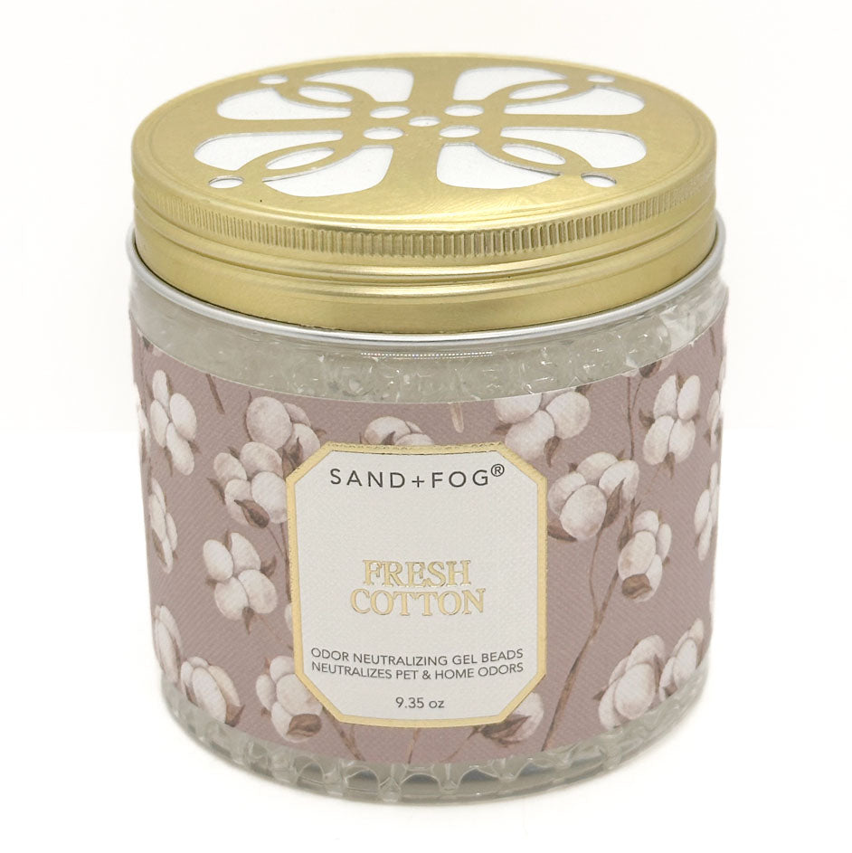 A glass jar of Sand+Fog Fresh Cotton odour neutralising gel beads with a gold metal lid and a dusty pink label decorated with cotton bolls.