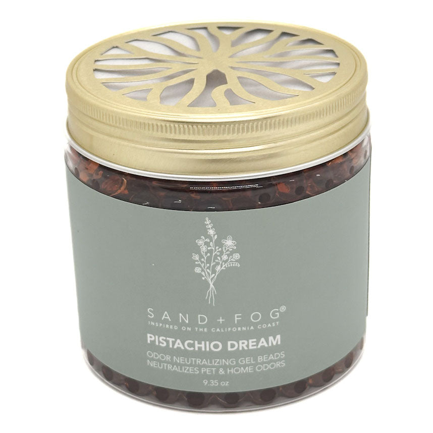 A jar of Sand + Fog Pistachio Dream odour neutralising gel beads, featuring a metallic gold lid with a decorative cutout and a muted grey-green label.