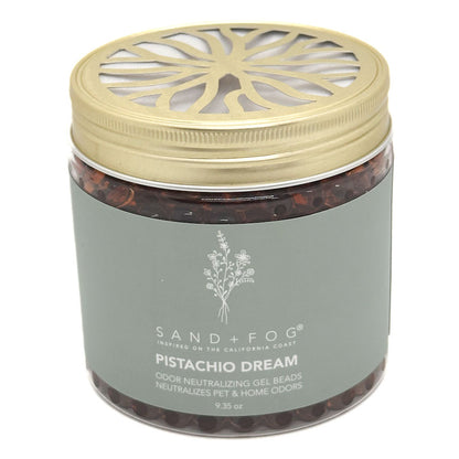A jar of Sand + Fog Pistachio Dream odour neutralising gel beads, featuring a metallic gold lid with a decorative cutout and a muted grey-green label.