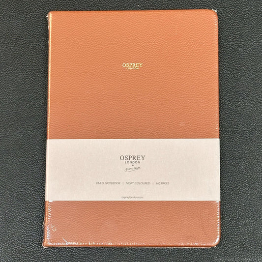 An Osprey London lined notebook in a peachy orange textured leather cover, wrapped in clear plastic and featuring a white paper band label around the middle.