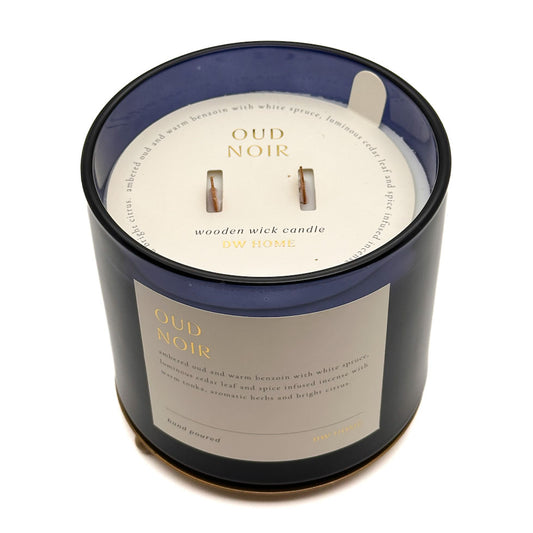 A dark blue glass jar candle with a cream-coloured label and wick insert, photographed on a clean white background. The label reads 'OUD NOIR' and 'wooden wick candle ON HOME'.