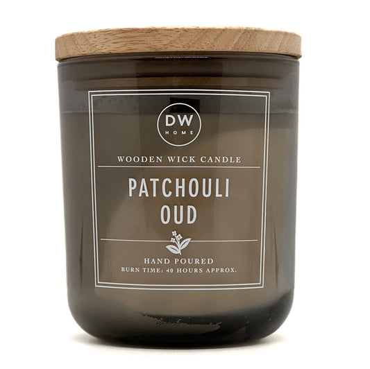 A dark amber glass jar candle with a light natural wood lid and a white label reading 'DW HOME' and 'PATCHOULI OUD'.