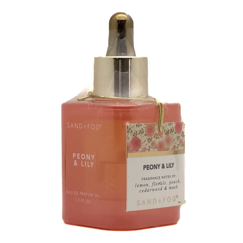 Sand + Fog Peony & Lily fragrance oil in a square amber-brown bottle with a gold-tone dropper cap, featuring a floral label and hanging tag on a white background.