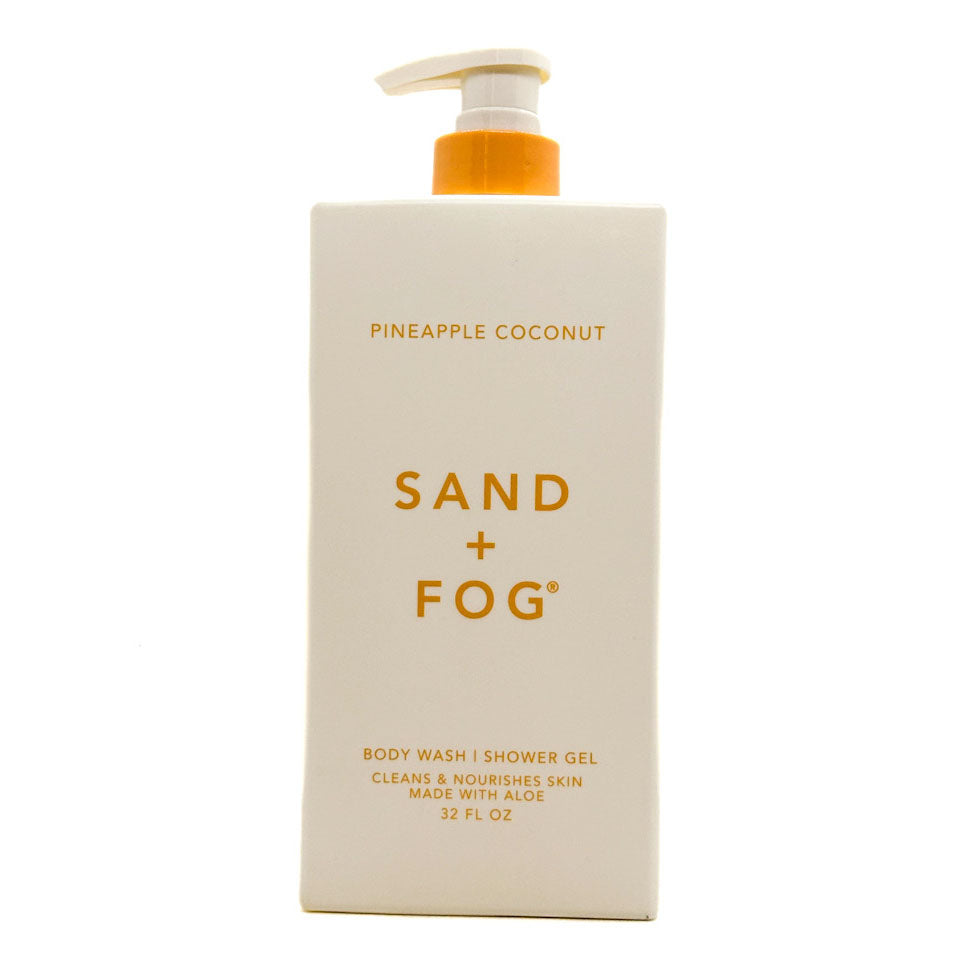 A 32 fl oz pump bottle of Sand + Fog Body Wash in Pineapple Coconut scent, featuring a cream-colored rectangular bottle with gold lettering and an orange pump dispenser, set against a plain white background.
