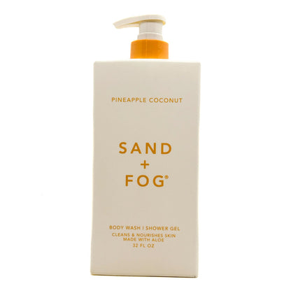 A 32 fl oz pump bottle of Sand + Fog Body Wash in Pineapple Coconut scent, featuring a cream-colored rectangular bottle with gold lettering and an orange pump dispenser, set against a plain white background.