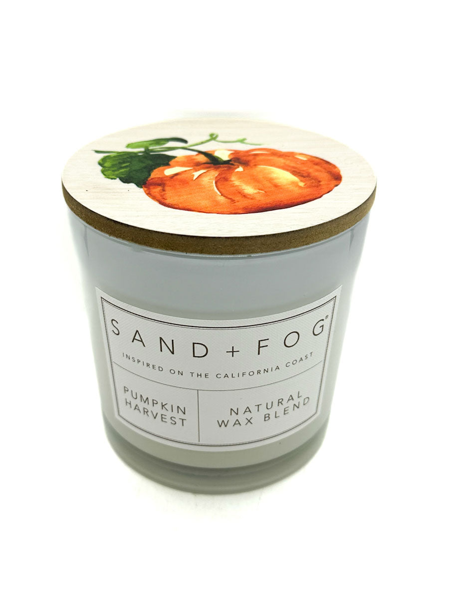 Candle with a pumpkin design on the lid and 'Sand + Fog' branding.