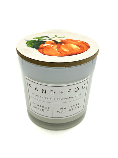 Candle with a pumpkin design on the lid and 'Sand + Fog' branding.