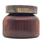 A Pumpkin brulee ribbed amber glass jar with a dark brown textured lid featuring the brand name 'DW HOME' in gold lettering, set against a plain white background.