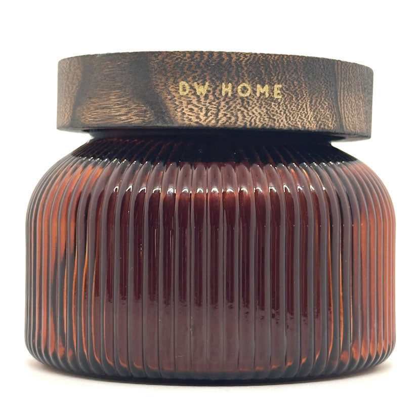 A Pumpkin brulee ribbed amber glass jar with a dark brown textured lid featuring the brand name 'DW HOME' in gold lettering, set against a plain white background.