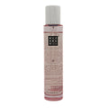 A clear cylindrical bottle of The Ritual of Sakura cherry blossom hair & body mist, containing a pink liquid, featuring a white cap and a black label with white text that reads 'RITUALS'. The bottle is centered against a plain white background.