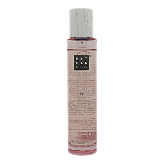 A clear cylindrical bottle of The Ritual of Sakura cherry blossom hair & body mist, containing a pink liquid, featuring a white cap and a black label with white text that reads 'RITUALS'. The bottle is centered against a plain white background.