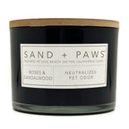 Roses & Sandalwood Black candle with a wooden lid labeled 'Sand + Paws' on a white background