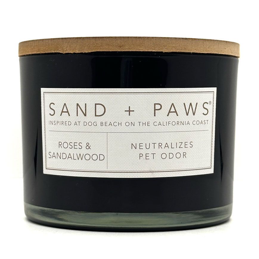 Roses & Sandalwood Black candle with a wooden lid labeled 'Sand + Paws' on a white background