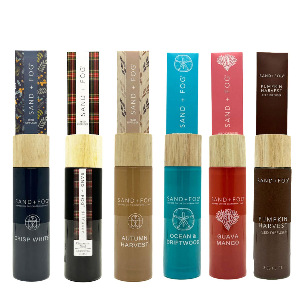 Collection of Sand + Fog reed diffuser bottles with various designs and colours on a white background.