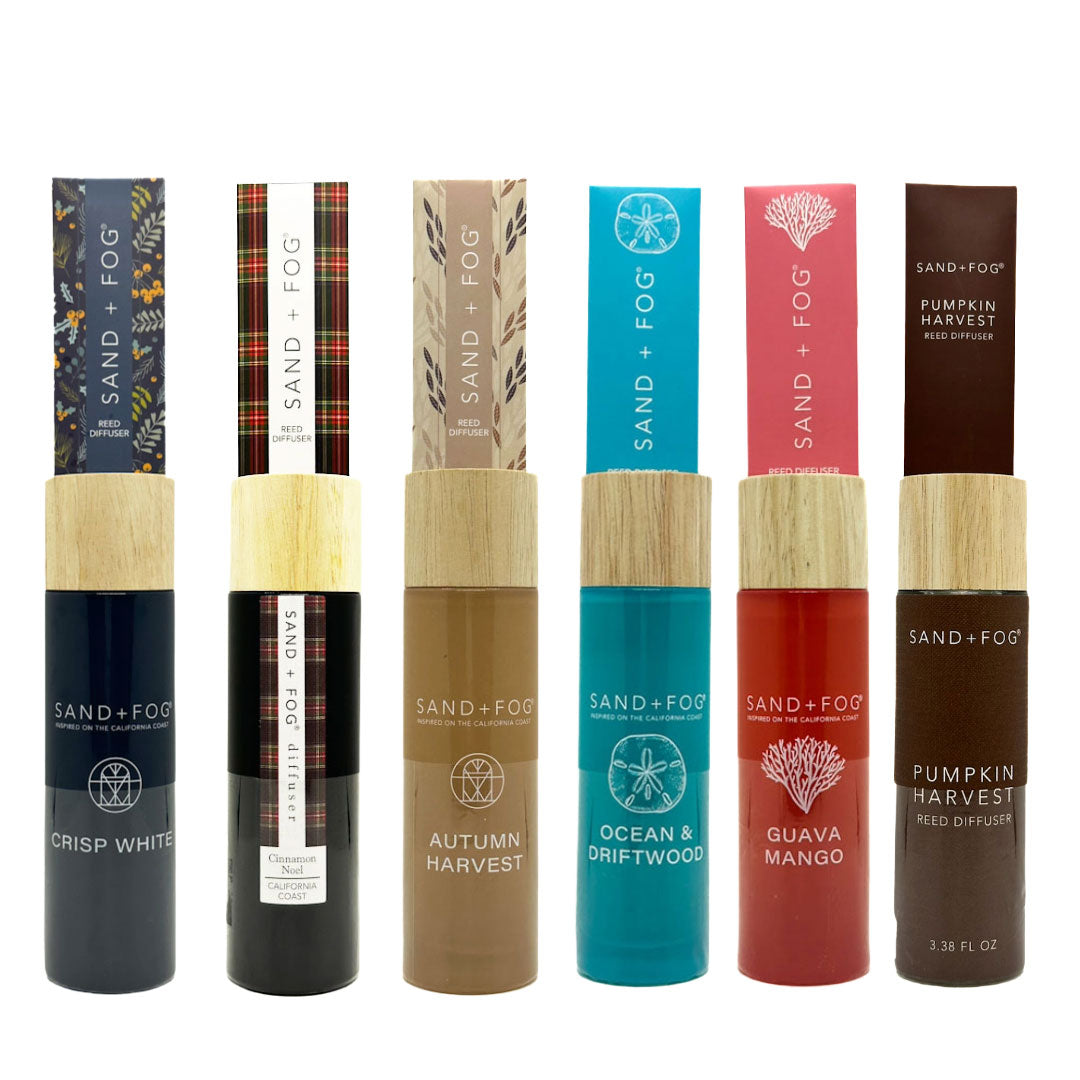 Collection of Sand + Fog reed diffuser bottles with various designs and colours on a white background.