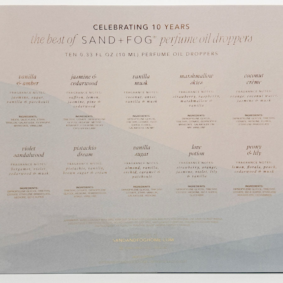The back of a Sand + Fog perfume oil droppers box celebrating 10 years of the product, featuring a grid of ten different fragrance names and descriptions in a light beige color on a white background.