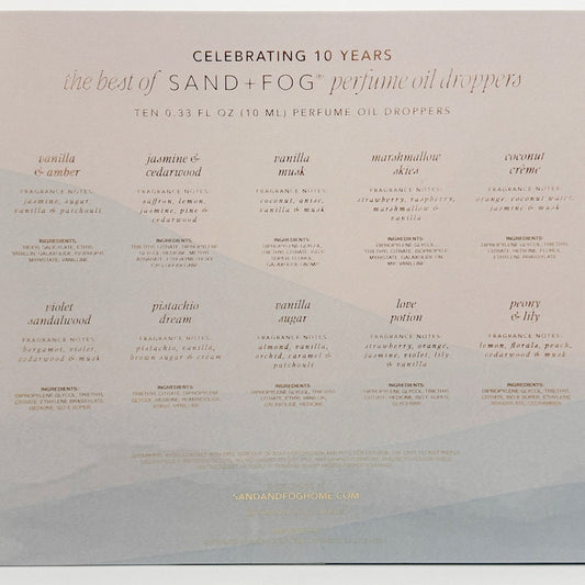 The back of a Sand + Fog perfume oil droppers box celebrating 10 years of the product, featuring a grid of ten different fragrance names and descriptions in a light beige color on a white background.