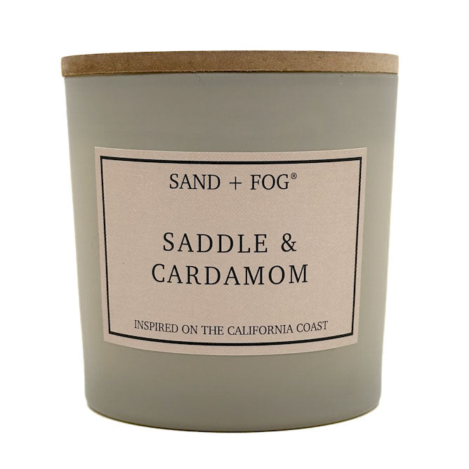 Candle with 'Saddle & Cardamom' label by SAND + FOG on a white background