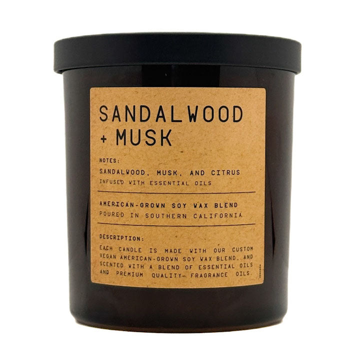 A Leoben Company dark amber glass jar candle with a black lid and a tan paper label reading 'SANDALWOOD + MUSK' on a white background.