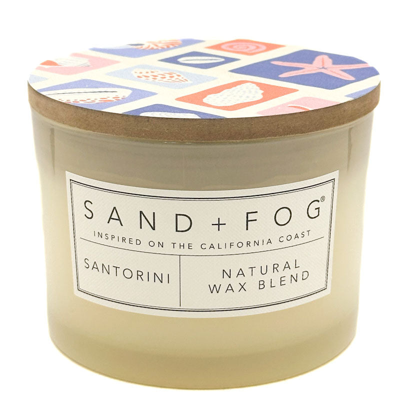 Santorini candle with a patterned lid labeled 'Sand + Fog' on a white background
