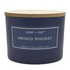 Navy blue candle with a wooden lid labeled 'Sand + Fog Smoked Whiskey' on a white background