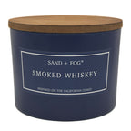 Navy blue candle with a wooden lid labeled 'Sand + Fog Smoked Whiskey' on a white background
