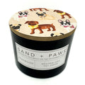 Teakwood candle with a lid featuring dog illustrations and 'Sand + Paws' branding.