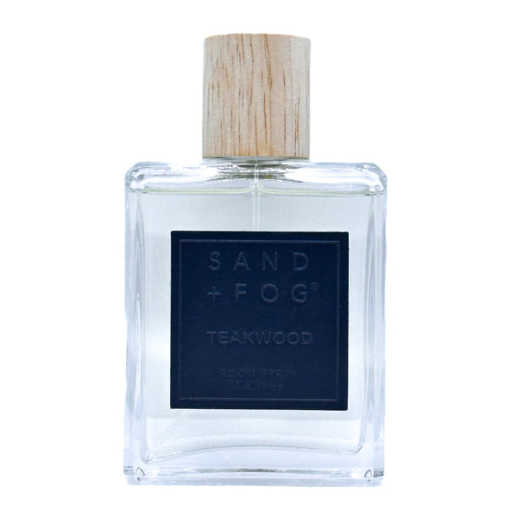 Clear bottle of Sand + Fog Teakwood room spray with a wooden cap on a white background