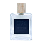 Clear bottle of Sand + Fog Teakwood room spray with a wooden cap on a white background