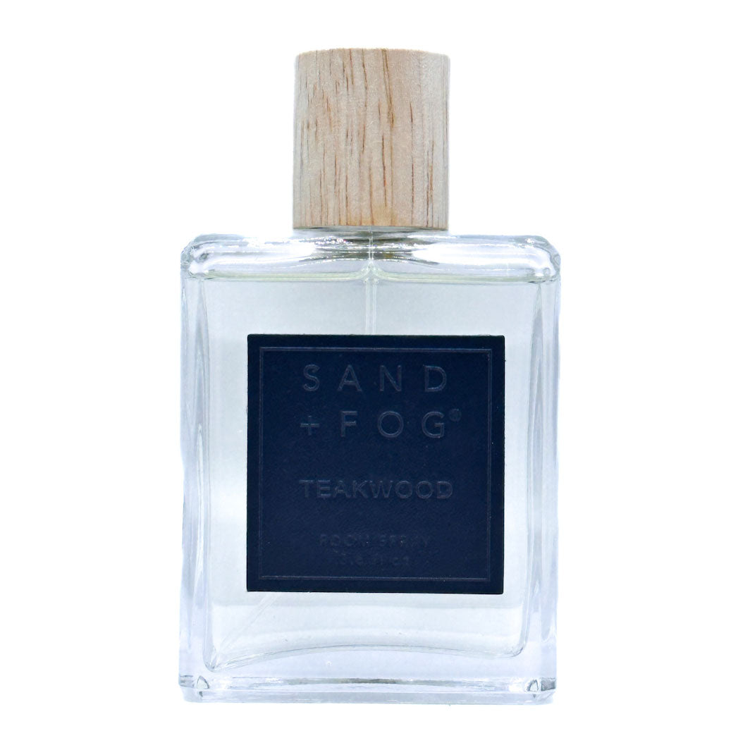 Clear bottle of Sand + Fog Teakwood room spray with a wooden cap on a white background