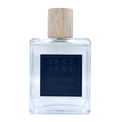 Clear bottle of Sand + Fog Teakwood room spray with a wooden cap on a white background