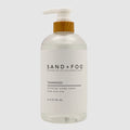 Clear SAND + FOG Teakwood hand soap bottle with pump and wooden top on a light grey background