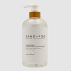 Clear SAND + FOG Teakwood hand soap bottle with pump and wooden top on a light grey background